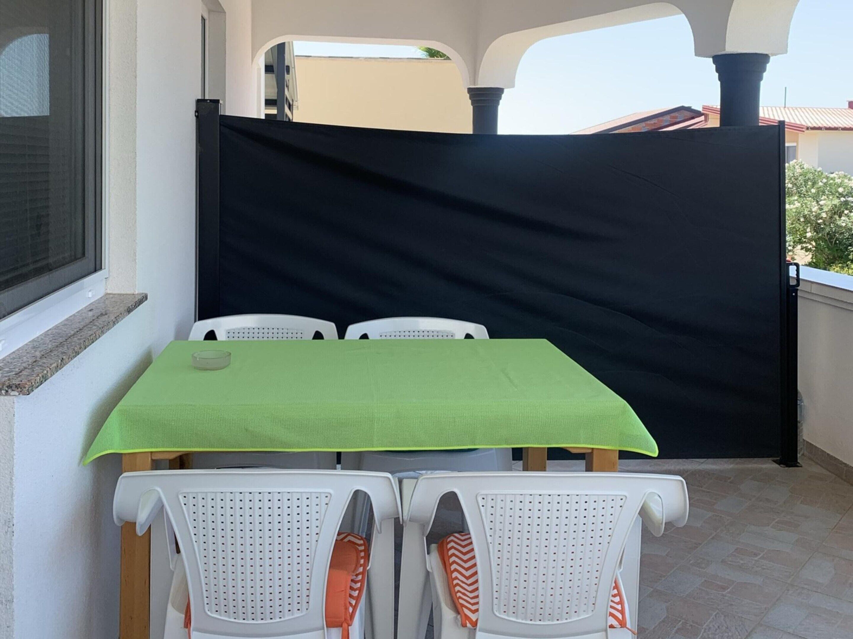 A patio area with a table and chairs, a black privacy screen, and a window.