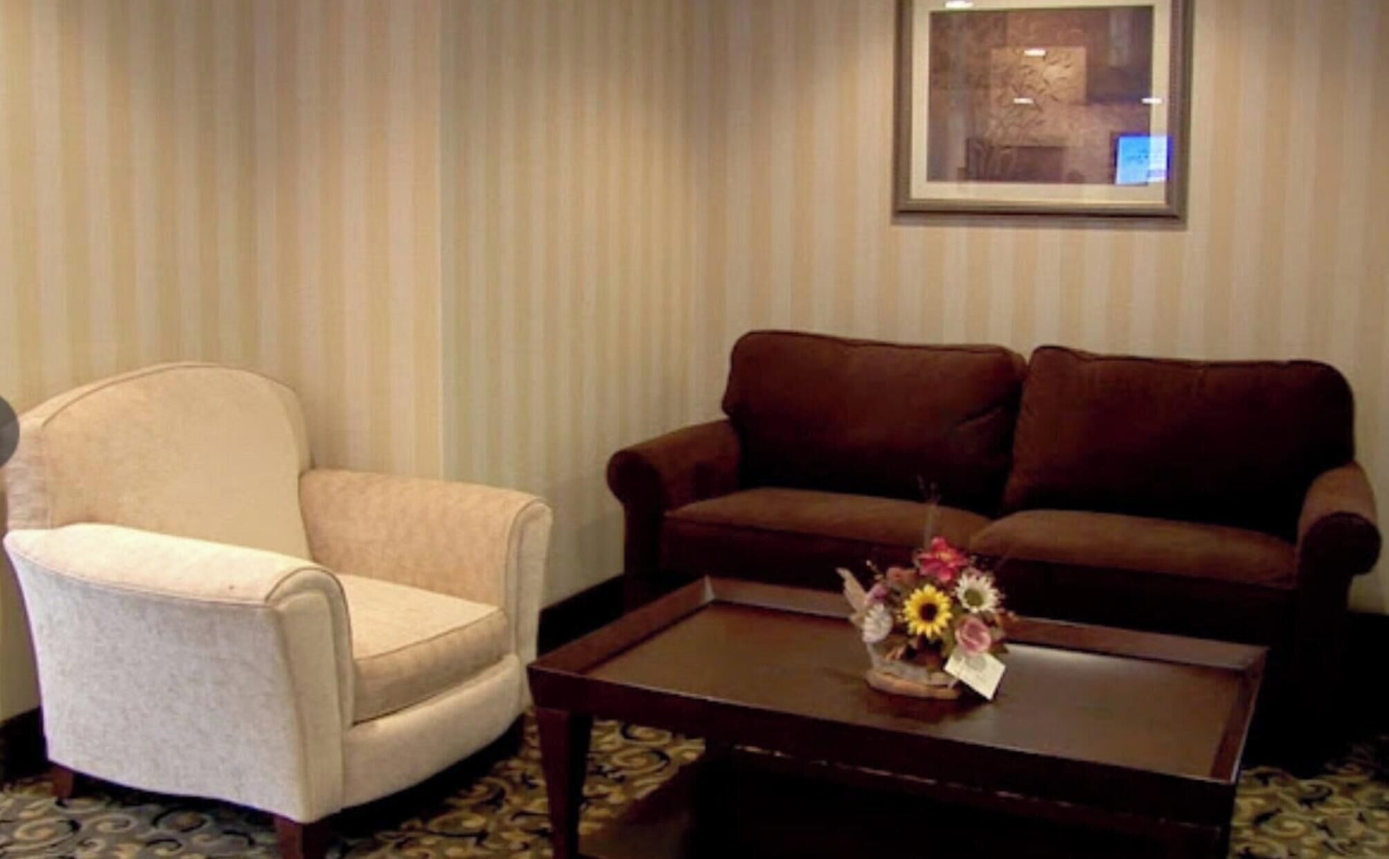 A room with a beige armchair, a brown sofa, and a coffee table with a floral arrangement.