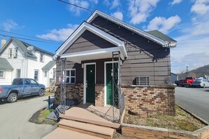 A small single-story house with a front porch, a brick foundation, and a garage door. - 2 Bedroom Cabin|East Stroudsburg (East Stroudsburg)