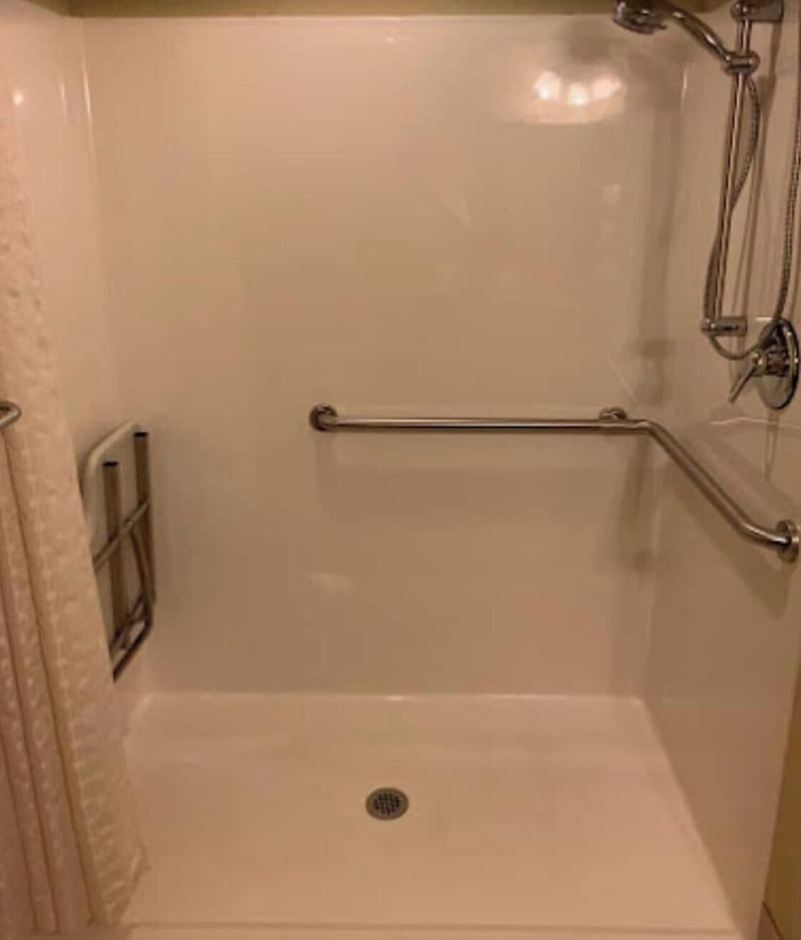 A shower with a grab bar, a showerhead, and a drain.