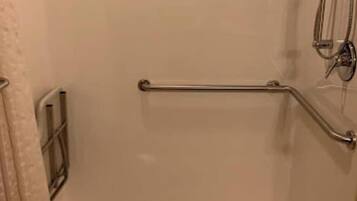 A shower with a grab bar, a showerhead, and a drain.
