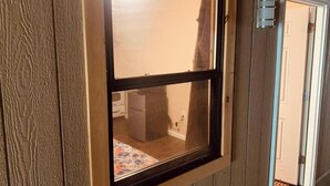 Una ventana con marco de madera que ofrece vista a una cocina, incluyendo un refrigerador y una encimera.