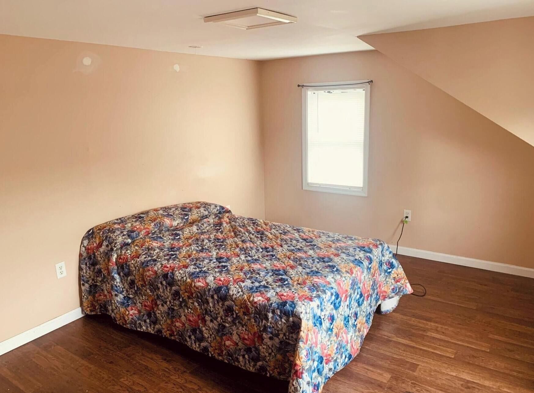Een slaapkamer met een bed, een raam en een schuine kap.