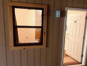 Una habitación con un panel de madera en la pared, una ventana con marco negro y una puerta blanca con placa de número.