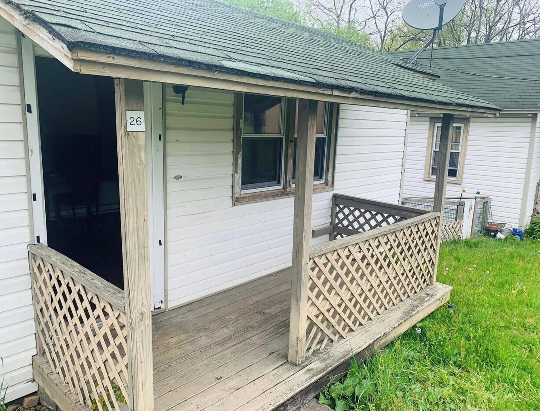 A single-story house with a porch, a number '26' sign, and a satellite dish.