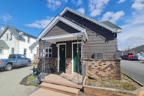 A small single-story house with a front porch, a brick foundation, and a garage door. - Studio with Kitchen|East Stroudsburg (East Stroudsburg)