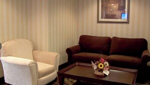 Una habitación con un sillón color beige, un sofá marrón y una mesa de centro con un arreglo floral.