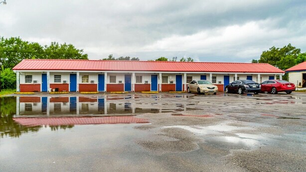 Un motel con techo rojo, varias habitaciones y un estacionamiento con coches.