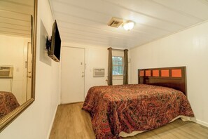 Een slaapkamer met een bed, spiegel, televisie en raam.