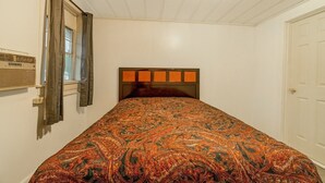 Un dormitorio con cama, ventana con cortinas, radiador y puerta.