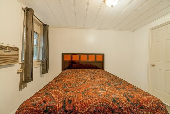 A bedroom with a bed, a window with curtains, a radiator, and a door.