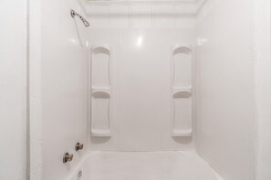 Una bañera blanca con cabezal de ducha, dos estantes integrados y desagüe.