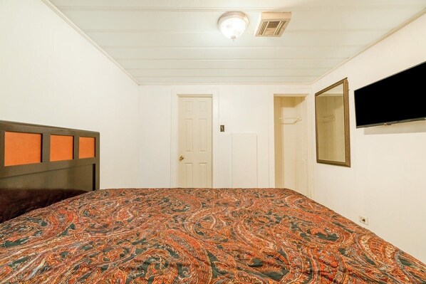 A bedroom with a patterned bedspread, a headboard, a television mounted on the wall, and a door.