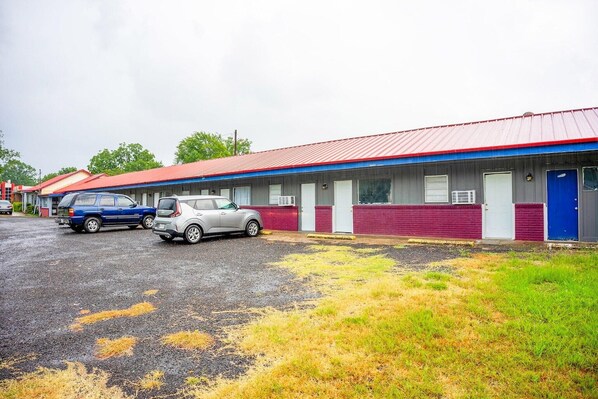 Un motel avec un toit rouge et une porte bleue. Deux voitures sont garées devant.