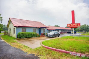A motel with a red roof and a 'Motel' sign, a car parked in front, and a 'No Parking Fire Lane' sign.
