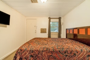 A bedroom with a bed, a television mounted on the wall, a window with curtains, and a door.