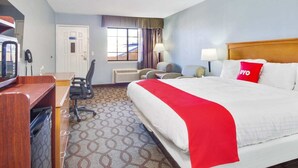 Ein Hotelzimmer mit Bett, Schreibtisch, Stuhl und einem fenster mit Vorhängen.
