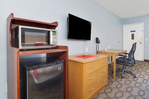 Una habitación compacta con microondas, refrigerador, escritorio de madera, silla y televisor de pantalla plana montado en la pared.