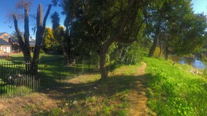 Ein von einer Mauer umgebener Garten mit einem Weg, ein Gebäude mit grauem Dach und ein Fluss.