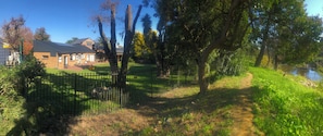 A fenced garden with a pathway, a building with a grey roof, and a river. - Elegant two-bedroom hideaway in picturesque Stellenbosch. (Stellenbosch)