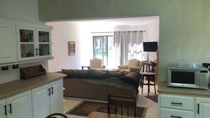Ein Wohnzimmer mit einer Couch, Sesseln, einem Esstisch, Küchenschränken und einem Fernseher.