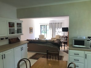 A living room with a sofa, chairs, a dining table, kitchen cabinets, and a TV. - Elegant two-bedroom hideaway in picturesque Stellenbosch. (Stellenbosch)