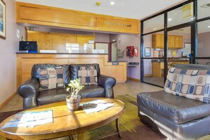 A reception area with a wooden counter, two leather sofas with patterned cushions, a coffee table with a plant, and a glass door leading to a kitchen. - Cape Coral FL | King bed (Ingleside TX)