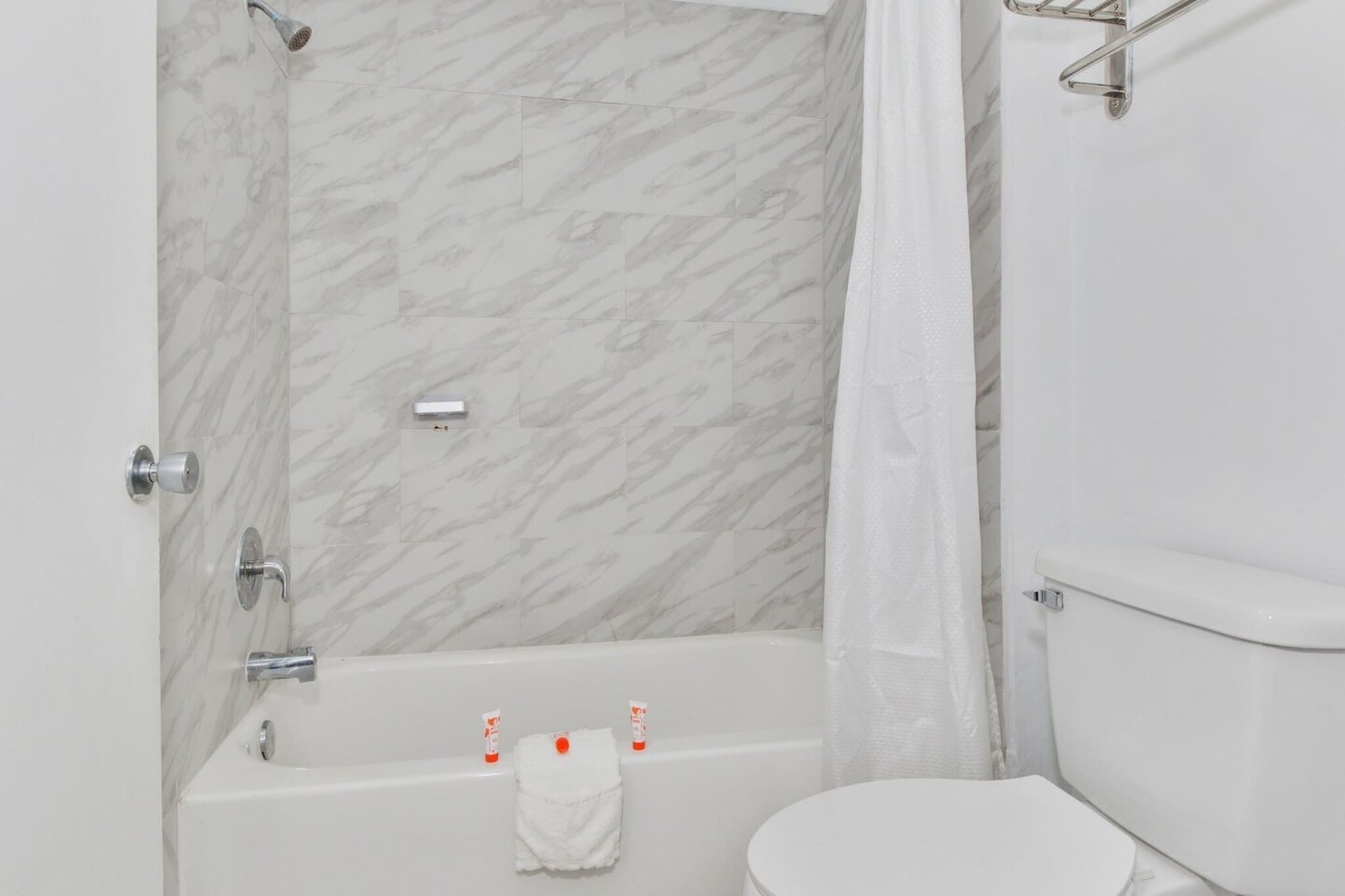 A bathroom with a marble wall, a bathtub, a toilet, and a shower curtain.