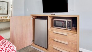 Una kitchenette compacta con refrigerador, microondas y un televisor montado en la pared.