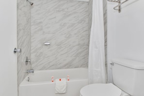 Une salle de bain avec un mur en marbre, une baignoire, des toilettes et un rideau de douche.