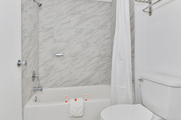 Une salle de bain avec un mur en marbre, une baignoire, des toilettes et un rideau de douche.