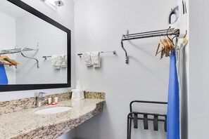 Une salle de bain avec un lavabo doté d’un plan de travail en granit, un miroir, des porte-serviettes et un rideau de douche.