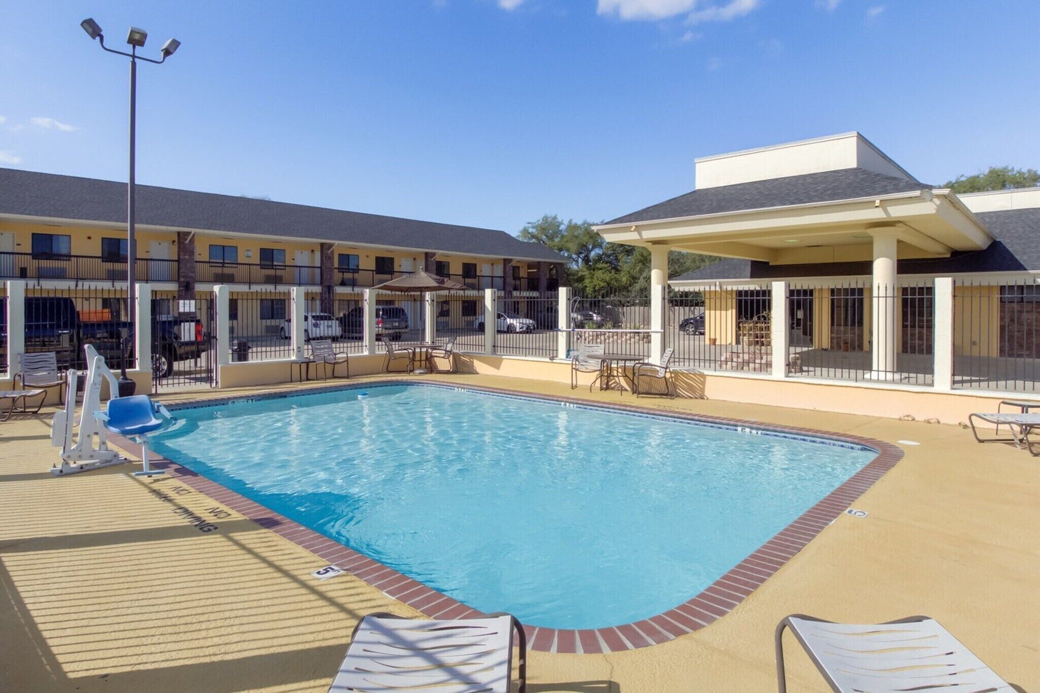 A swimming pool with lounge chairs, a covered seating area, and a building with multiple windows and balconies.