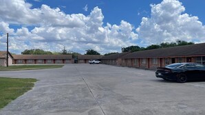 Un motel doté d’un grand parking, d’une rangée de chambres et surplombant un ciel bleu dégagé.