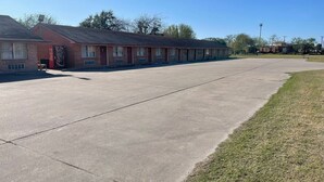 Un motel avec une longue rangée de chambres, un parking et une zone herbeuse.