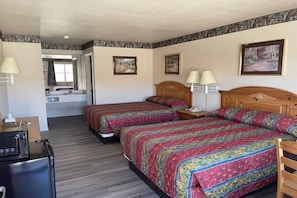 A hotel room with two beds, a desk, a chair, a mirror, and a bathroom visible through an open door. - 2 Queen Bed | Smoking (Mathis, TX)
