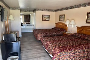 A hotel room with two beds, a desk with a television, and a bathroom visible through an open door.