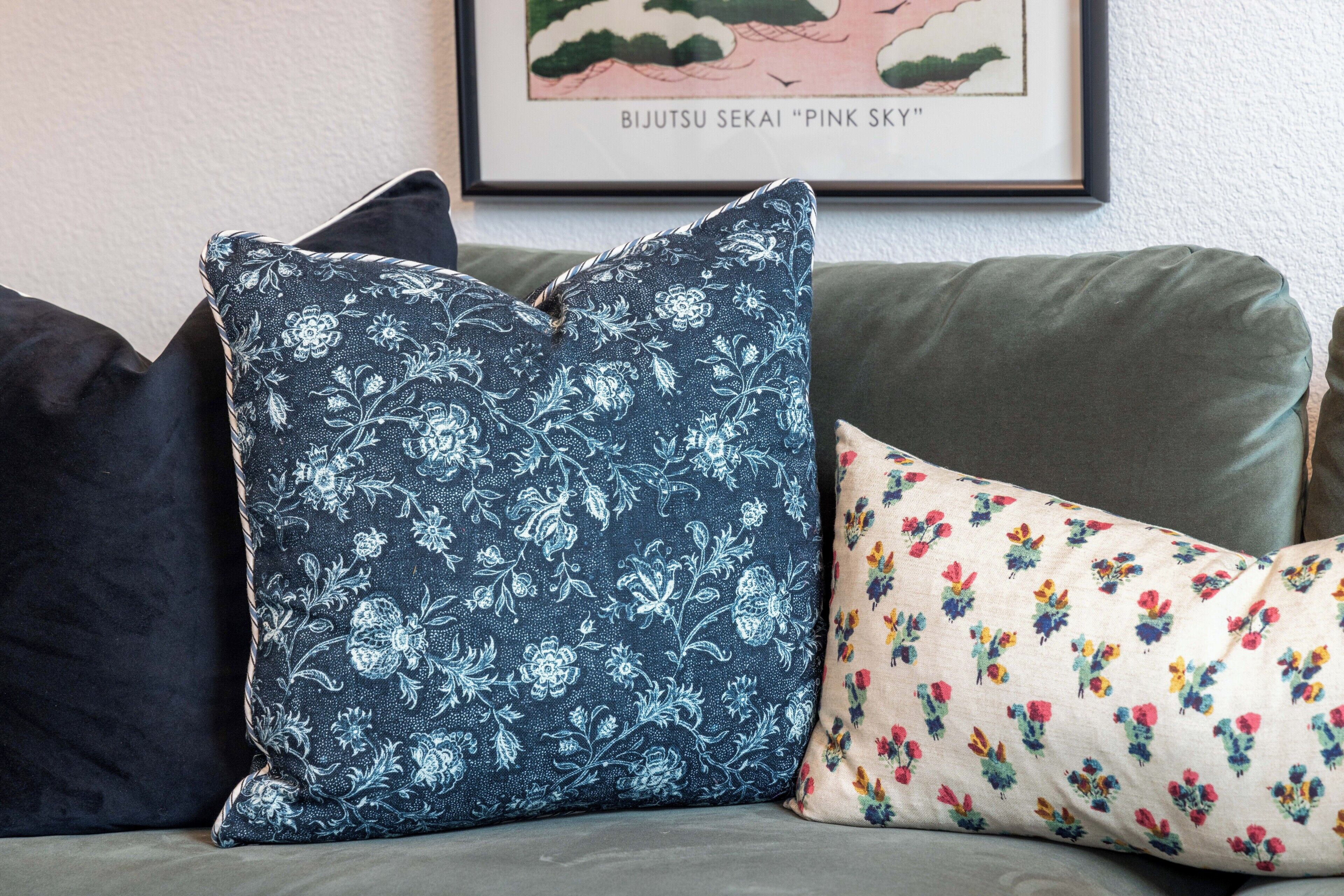 A sofa with three pillows, one with a floral pattern, one with a paisley pattern, and one with a multicolored floral pattern.