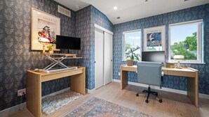 A modern home office with two desks, a television, and framed artwork on the walls.