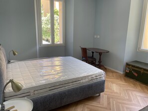 A bedroom with a bed, a desk, a chair, a window, and a chest of drawers.