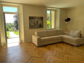 A living room with a beige sectional sofa, a painting on the wall, and a floor lamp. - The Garden Apartment in a Restored 20th-Century Villa (Caslino D'erba)