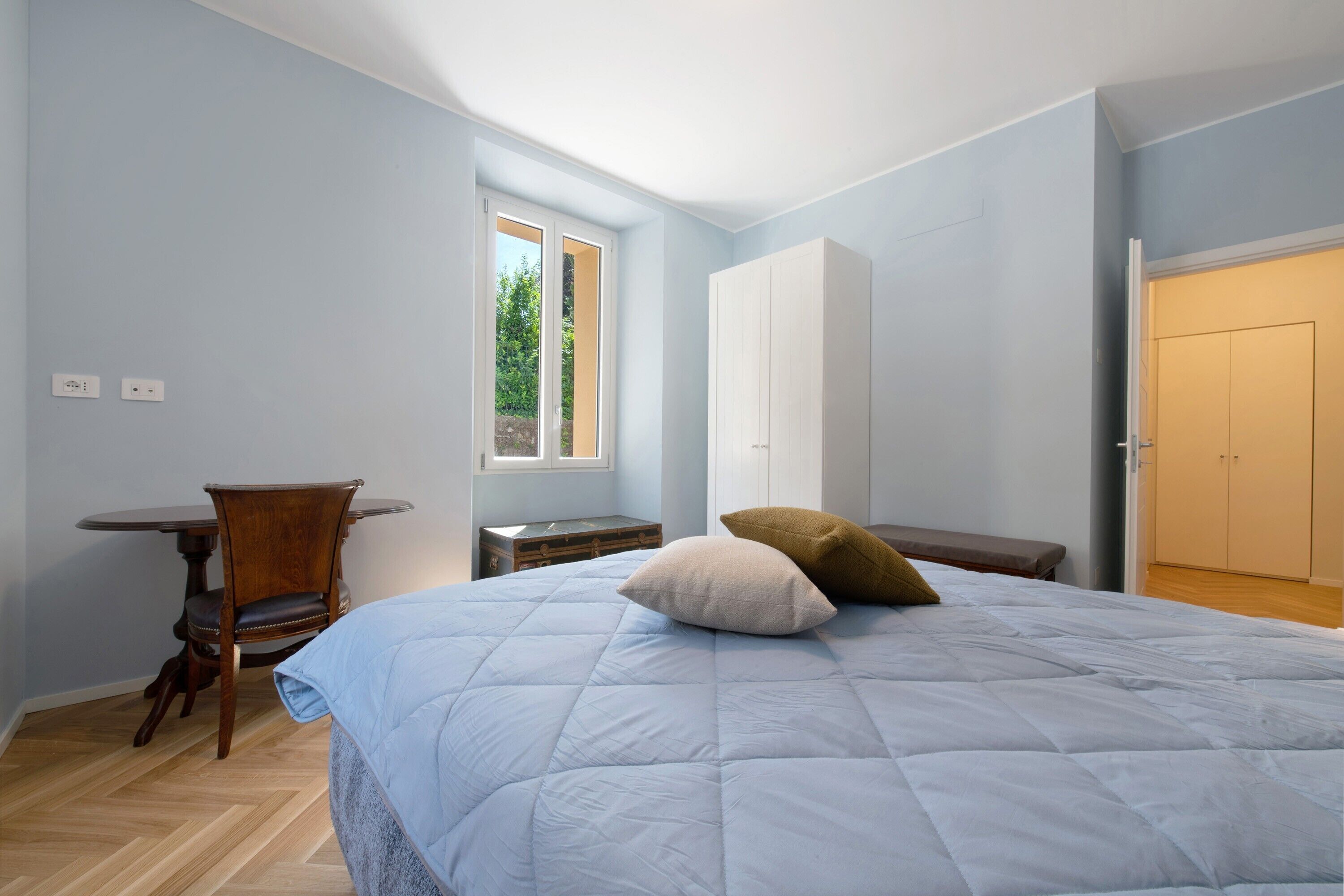 Ein Schlafzimmer mit Bett, Sessel, Nachttisch, Kleiderschrank und Fenster.
