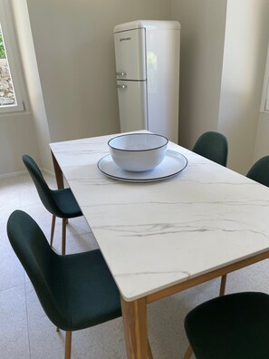 A dining table with a bowl on a plate, surrounded by chairs, and a white appliance in the background.