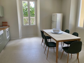A kitchen with a dining table, chairs, a refrigerator, and a window with a view of greenery. - The Garden Apartment in a Restored 20th-Century Villa (Caslino D'erba)