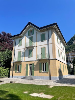 A multi-story building with balconies, a stone-paved entrance, and a well-maintained lawn. - The Garden Apartment in a Restored 20th-Century Villa (Caslino D'erba)