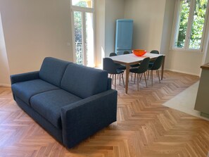 Et værelse med en blå sofa, et spisebord med stole, et blå skab og et fiskebensparket trægulv.