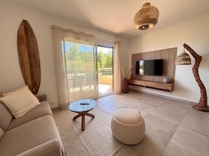 Ein modernes Wohnzimmer mit einer Couch, einem runden Hocker, einem kleinen runden Tisch und einem an einer Holzpaneelwand montierten Fernseher.