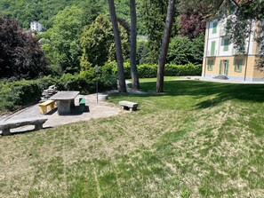 A park with stone benches, a stone table, and a building with green shutters.