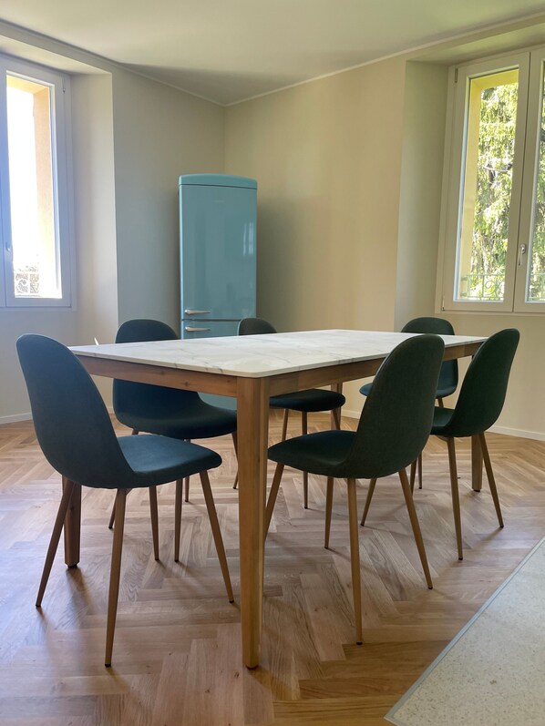 A room with a wooden herringbone floor, a rectangular table with six chairs, and a blue cabinet.