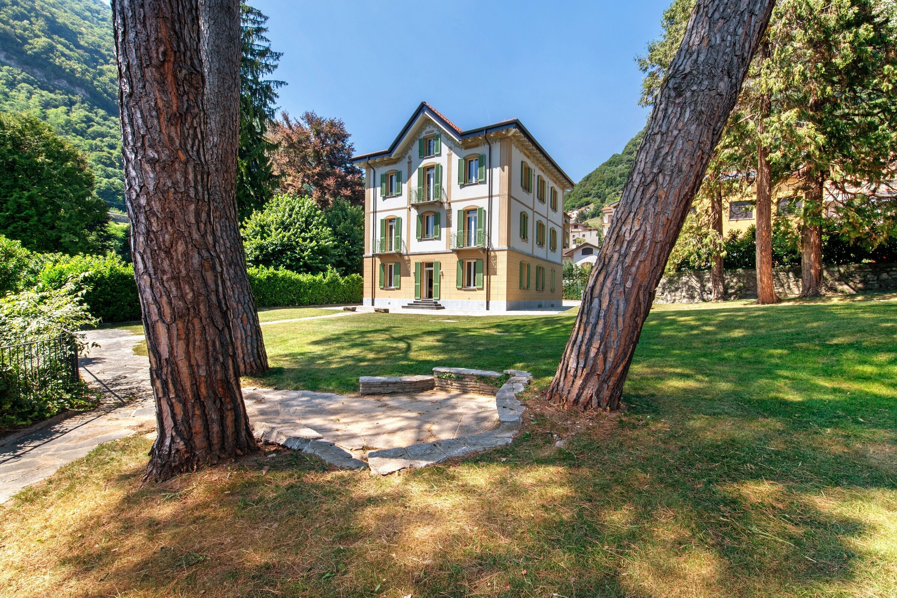 A multi-story building with a symmetrical facade, a central entrance, and a surrounding grassy area with trees.
